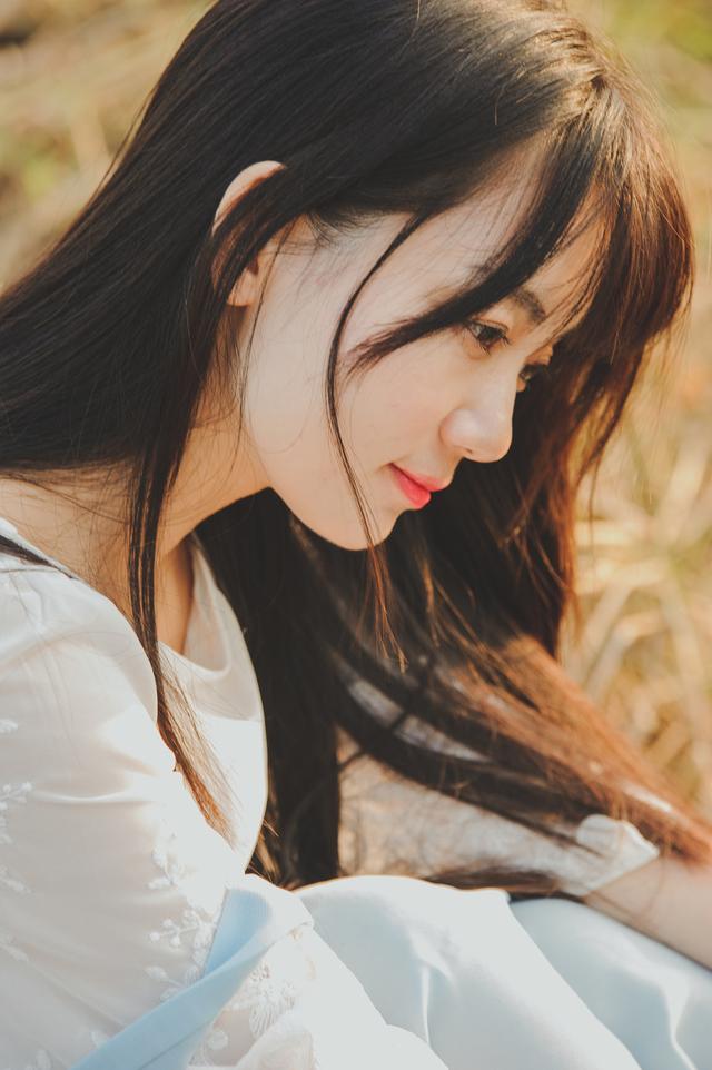 美丽的中国年轻女孩的肖像穿着白色的婚纱坐在紫色的薰衣草花的白色长凳上她的草帽在膝盖上微笑在她的_美女照片